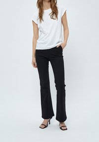 Vit kortärmad t-shirt kombinerad med svarta utställda byxor, med en slät yta och en figurnära design. Svarta sandaletter med hög klack fulländar looken.