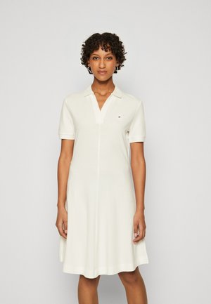 Abito polo a maniche corte in cotone bianco, con scollo a V, colletto strutturato e logo del marchio discreto sul petto, dotato di una gonna svasata.