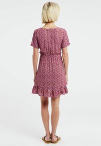 Vestido de manga corta, hasta la rodilla, en tejido rosa con un patrón floral, cintura elástica y dobladillo con volantes. Sandalias planas puestas.