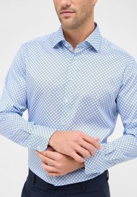 Camicetta azzurra a motivi con una vestibilità slim, caratterizzata da una piccola stampa geometrica, colletto button-down e polsini con bottone. Materiale in cotone.