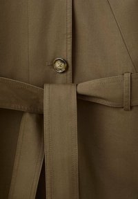 Gros plan sur un manteau marron avec un bouton et une ceinture en tissu assortie nouée à la taille.