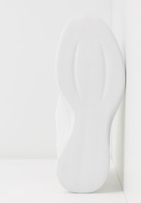 Semelle de sneaker blanche avec des stries diagonales et un motif de grip texturé. Forme arrondie, finition lisse et courbure subtile le long des bords.