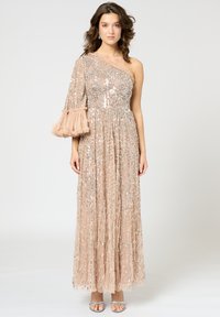 Robe de soirée longue, beige, avec une manche ornée, présentant des sequins et des franges. Texture fluide et plissée avec un corsage ajusté.
