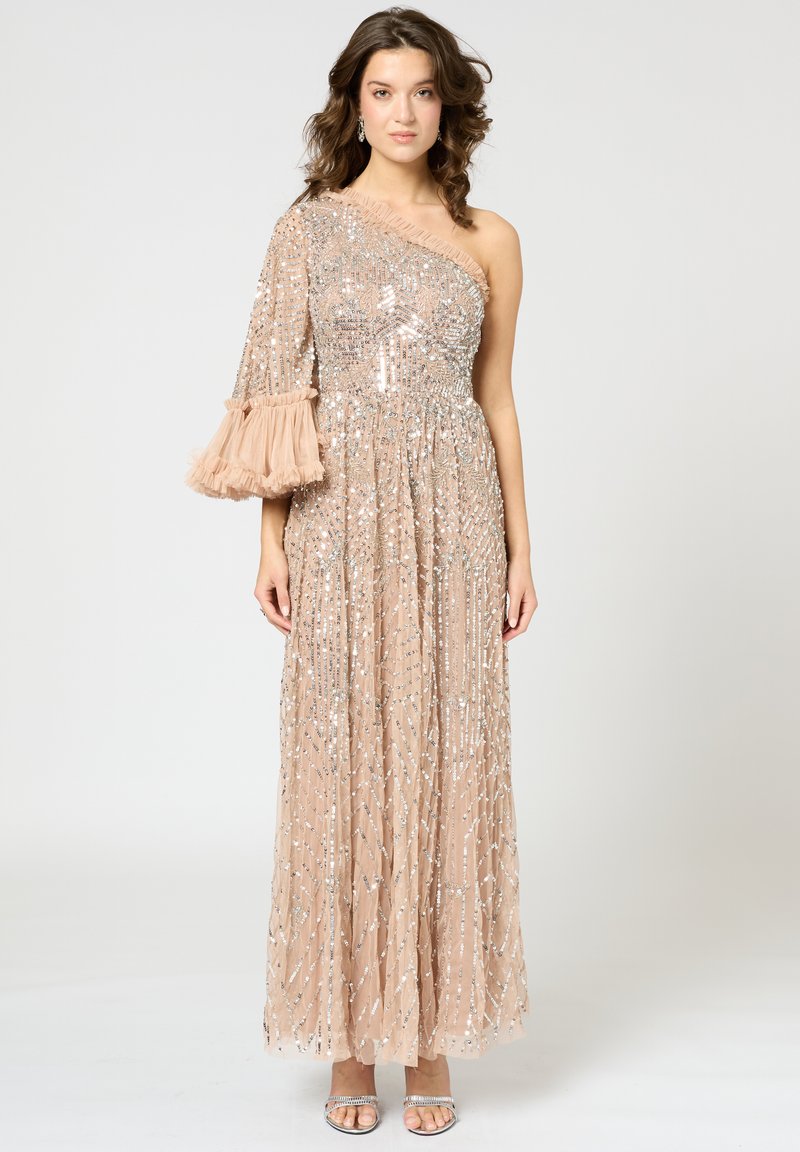 Robe de soirée longue, beige, avec une manche ornée, présentant des sequins et des franges. Texture fluide et plissée avec un corsage ajusté.