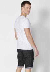 Tricou alb cu mânecă scurtă și guler rotund, asociat cu pantaloni scurți din denim negru, de lungime până la genunchi, având buzunare laterale și margini răsucite.