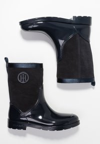 Laivastonsiniset sadetossut, joissa kiiltävä kumipohja ja mattapintainen mokkanahkainen yläosa. Varustettu logolla, kontrastisilla materiaaleilla ja kuvioidulla pohjalla pitoja varten.