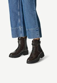 Black and brown patterned ankle boots with laces, side zippers, and thick rubber soles, paired with light blue wide-leg denim pants.