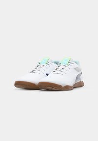 White athletic shoes with gum sole, silver accents, mesh tongue, and light blue highlights. Features laces and branding on tongue.