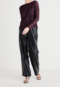 Haut en dentelle bordeaux à manches longues avec un motif texturé, associé à un pantalon large en faux cuir noir et des talons à lanières noirs.