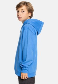 Sudadera azul con mangas largas, bolsillo canguro y capucha con cordón. Hecha de una tela suave, cuenta con puños y dobladillo acanalados.