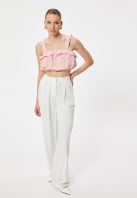 Top corto de cuadros vichy rosa y blanco con detalles de volantes, combinado con pantalones blancos de cintura alta. Tejido elegante y zapatos blancos de punta.