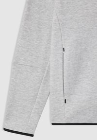 Felpa grigia con una texture liscia, caratterizzata da un accento nero all'orlo e un dettaglio con tasca laterale a sinistra.