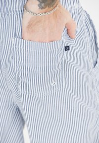 Blå- och vitrandiga byxor med ficka, som har en liten "CZ"-logotag. Materialet verkar lätt och andningsbart.