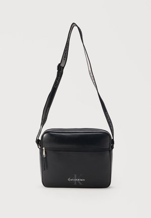 Μαύρη ορθογώνια τσάντα crossbody με μπροστινή τσέπη με φερμουάρ, ρυθμιζόμενο λουράκι με λογότυπο Calvin Klein και ανάγλυφο λογότυπο στο μπροστινό πάνελ.