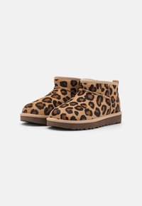 Bota de estampado de leopardo hecha de tejido texturizado con un puño color marrón, que presenta una suela plana de goma y un diseño de punta redondeada.