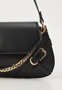 Černá kožená kabelka s hladkou texturou, zdobená zlatými řetízkovými doplňky a páskem se sponou. Design zahrnuje uzavření na klopu a strukturovaný tvar.