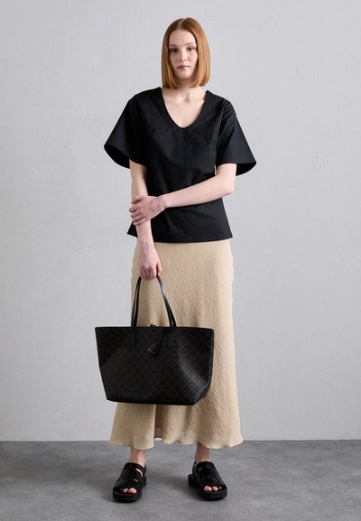 Black V-neck top with wide sleeves, paired with a textured beige skirt. Holding a black patterned tote bag and wearing black strappy sandals.