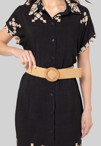 Zwarte jurk met beige bloemenborduursel op de kraag en mouwen, met knopen aan de voorkant en een brede gevlochten tan riem met een ronde gesp.