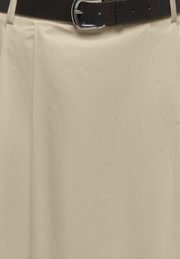 Beež seelik ees volditud detailidega, kinnitatud musta nahkvööga, millel on hõbedane pandel.