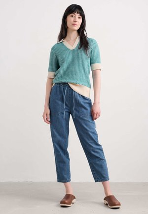 Pull en tricot turquoise avec un décolleté en V et des accents crème, associé à un pantalon en denim bleu clair à cordon de serrage et des sabots en bois marron.