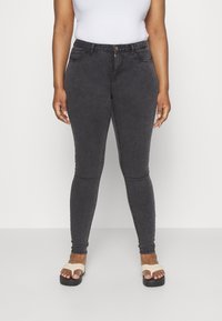 Jeans ajustados de mezclilla negra con una textura sutil, diseño de cinco bolsillos y un solo botón frontal. Llevados con flip-flops beige.