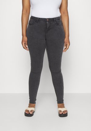 Jeans skinny de ganga preta com textura subtil, design de cinco bolsos e um único botão frontal. Usados com sandálias de dedo bege.