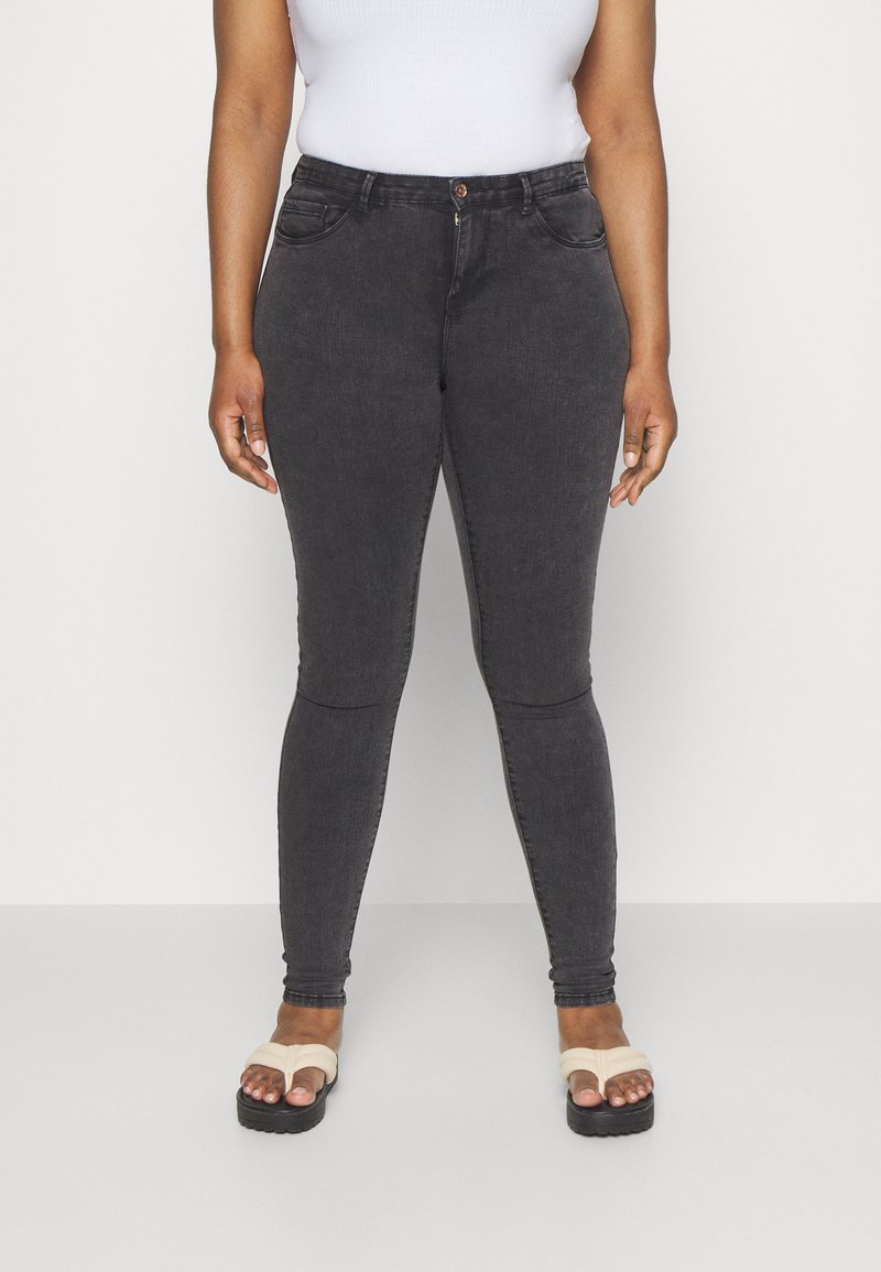 Jeans ajustados de mezclilla negra con una textura sutil, diseño de cinco bolsillos y un solo botón frontal. Llevados con flip-flops beige.