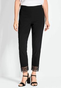 Zwarte broek met elastische tailleband en een gemêleerde zoom met een geometrisch uitgesneden patroon. Gecombineerd met zwarte hakken met bandjes.