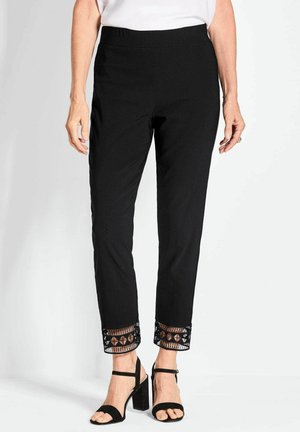 Pantaloni neri con cintura elastica e orlo testurizzato che presenta un motivo a ritaglio geometrico. Abb binati a scarpe con tacco a strappo nere.