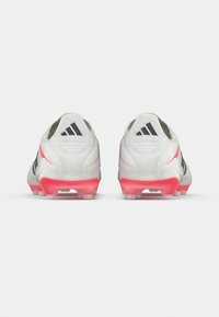 Λευκά ποδοσφαιρικά παπούτσια με υφή στην επάνω επιφάνεια, μαύρες λεπτομέρειες και σόλα με ροζ γραadiεντ. Διαθέτουν τρεις μαύρες ρίγες και μορφοποιημένα καρφιά.