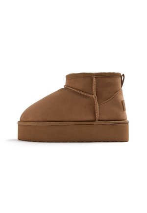 Stivali alla caviglia in suede marrone con punta arrotondata, cuciture rinforzate e suola piatta. Presentano un piccolo manico sul retro.