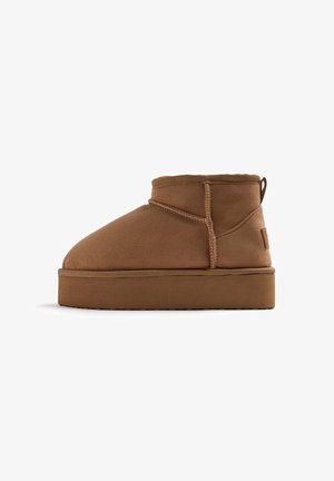 Stivali alla caviglia in suede marrone con punta arrotondata, cuciture rinforzate e suola piatta. Presentano un piccolo manico sul retro.