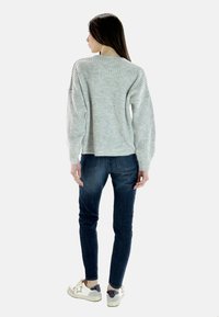 Maglione grigio chiaro a coste con maniche lunghe, vestibilità ampia, abbinato a jeans in denim scuro e sneakers bianche con dettagli a forma di stella.