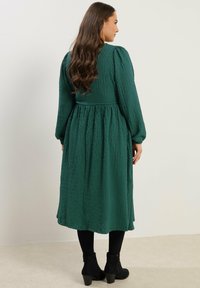 Lång, grön, strukturert klänning med puffärmar och samlad midja. Buren med svarta ankelboots med slät yta och blockklack.