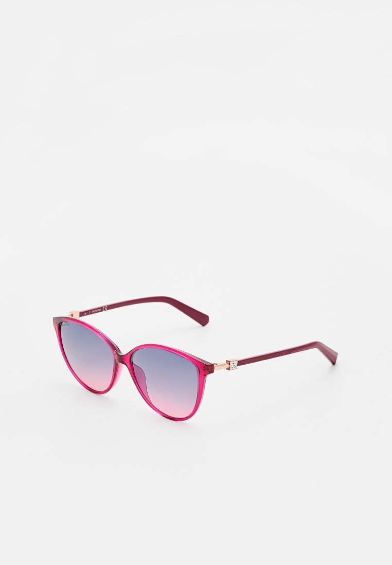 Lunettes de soleil en forme d'œil de chat avec des verres dégradés, présentant une monture rose et violette, des accents en métal doré et des branches fines.