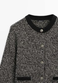 Cardigan en maille chinée noir et blanc avec col et poignets côtelés noirs, devant boutonné avec quatre boutons décoratifs argentés.