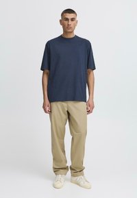 Tricou din bumbac bleumarin cu guler rotund, asortat cu pantaloni bej cu croială lejeră și teniși albi cu accente deschise. Design simplu și modern.