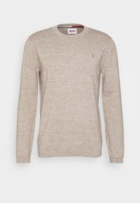 Beige långärmad stickad tröja med rund halsringning, med en liten logotyp på bröstet. Mjuk textur med ett subtilt mönster genom hela tröjan.