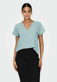 Blusa de manga corta en azul claro con escote en V y un ajuste ligeramente relajado, acompañada de una falda negra ajustada con rayas verticales.