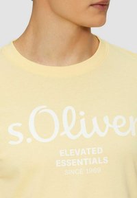 Short-sleeve yellow t-shirt made of cotton, featuring white printed text "s.Oliver Elevated Essentials Since 1969" on the front.