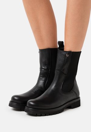 Stivali ankle in pelle nera con pannelli laterali elastici, punta rotonda, finitura testurizzata e suola in gomma resistente. Dotati di una linguetta sul tallone.