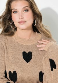 Maglione lavorato a maglia di colore beige, con motivi a cuore neri e soffici, collo e polsini a costine, maniche lunghe e vestibilità comoda.