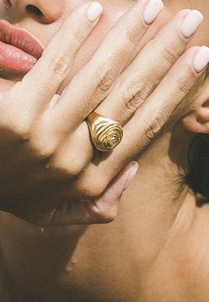 Gold ring designed to mimic a rose, with a textured surface. The ring is worn on a hand resting against the face.