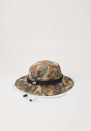 Kšiltovka v camo stylu vyrobená z textilu, s širokým okrajem, černým páskem s logem, nastavitelným provázkem a zemitými hnědými, zelenými a béžovými barvami.