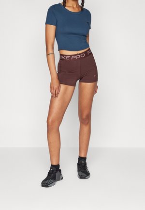 Brune Nike Pro shorts med en tekstureret talje, parret med en tætsiddende blå kortærmet top og sorte træningssko.