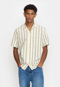 Korte mouwen overhemd in lichtcrème met marineblauwe verticale strepen, met knoopsluiting, relaxte pasvorm en zachte textuur, gecombineerd met blauwe denim jeans.