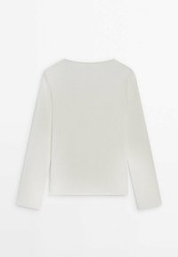Haut à manches longues blanc avec un col rond, fabriqué dans un tissu doux et lisse. Présente un design court et des détails de couture subtils.