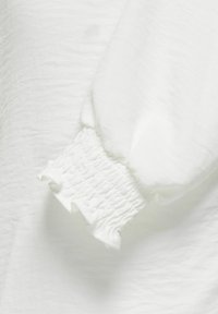 Weiße Bluse mit Puffärmel, gerüschtem elastischem Bündchen und Rüsche, gefertigt aus einem leichten, strukturierten Stoff.