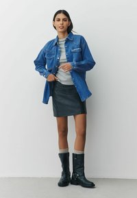 Denim shirt with button closures and two chest pockets, grey knit top, black leather mini skirt, and knee-high black boots with buckles.