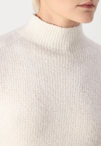 Ανοιχτόχρωμο πουλόβερ με λαιμόκοψη ζιβάγκο, με υφή που προσομοιάζει σε πλεκτό σχέδιο και ριμπ κολλέ. Το υλικό φαίνεται απαλό και ελαφρώς φουντωτό.